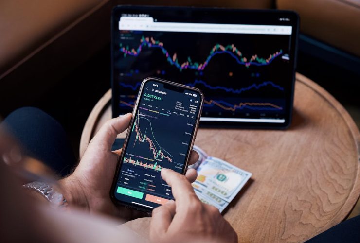 Close-up of a person trading stocks using a smartphone and a tablet.