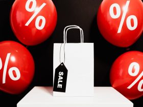 White shopping bag with sale tag surrounded by red balloons displaying percentage signs.