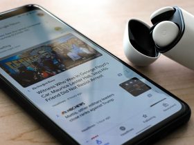 Close-up of a smartphone displaying news with wireless earphones on a table.