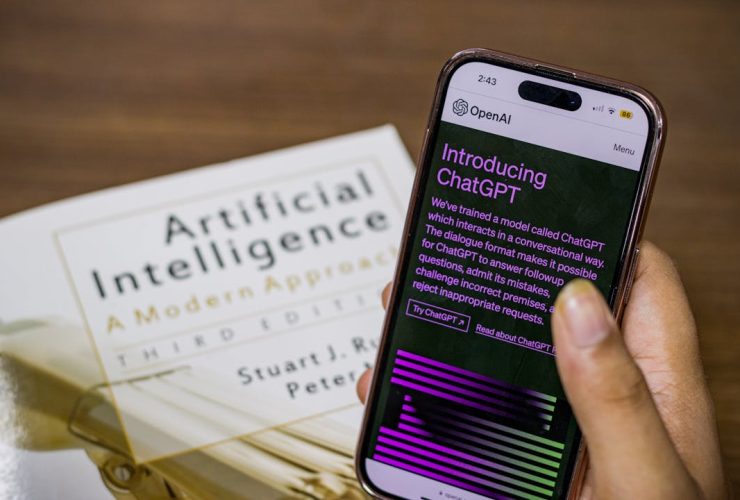 Close-up of a smartphone displaying ChatGPT app held over AI textbook.