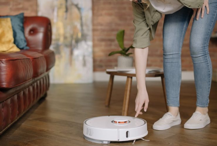 A woman in jeans interacts with a robotic vacuum cleaner in a cozy, stylish living room.
