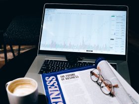 A modern business workspace featuring a laptop showing stock data next to a business magazine and coffee.