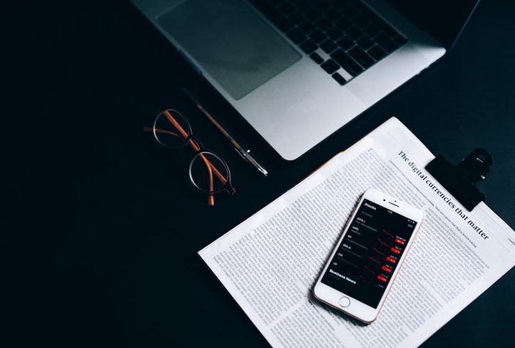 Flat lay of a digital workspace featuring a smartphone, glasses, and a laptop on a dark desk.