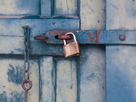 A close-up of a rusty padlock securing a blue painted wooden door with chain and bolt.