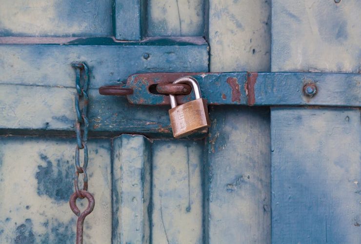 A close-up of a rusty padlock securing a blue painted wooden door with chain and bolt.