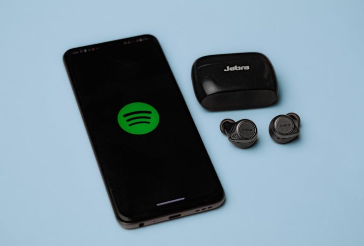 Closeup of Jabra true wireless earbuds with a smartphone displaying the Spotify app on a blue background.