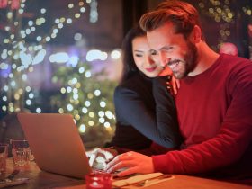 A couple using a laptop at a cozy restaurant with festive bokeh lights, enjoying online shopping together.
