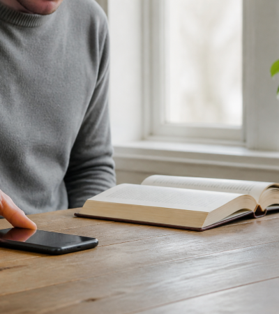 Una persona poggia lo smartphone sul tavolo per concentrarsi sulla lettura di un libro cartaceo, simbolo della Slow Tech.